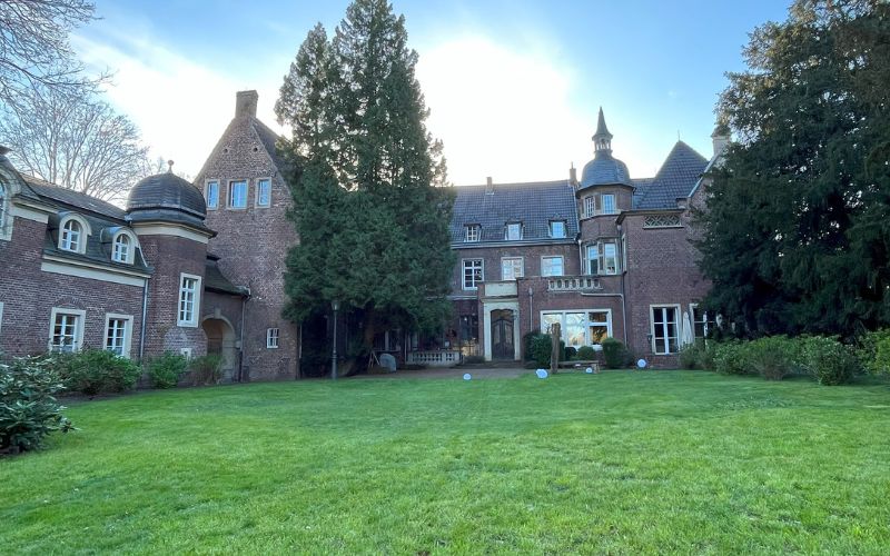 Schloss Elbroich in Düsseldorf-Holthausen mit einer Wiese im Vordergrund