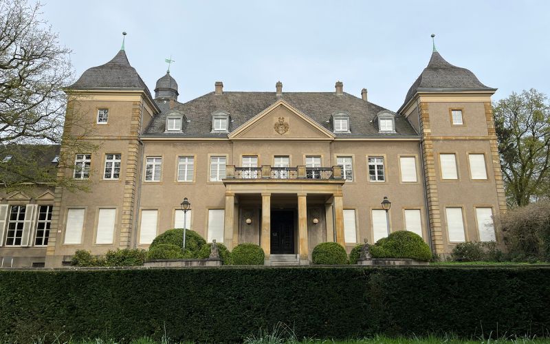 Schloss Garath bei klarem blauen Himmel und einer Hecke im Vordergrund